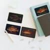 Four fish-themed cards on a white table next to a notebook and pen.