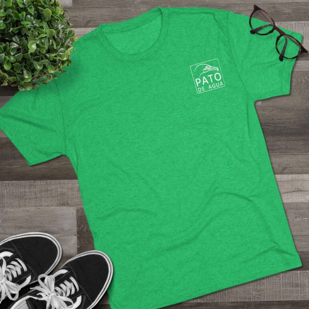 Green T-shirt with text and a pair of glasses on a wooden floor.