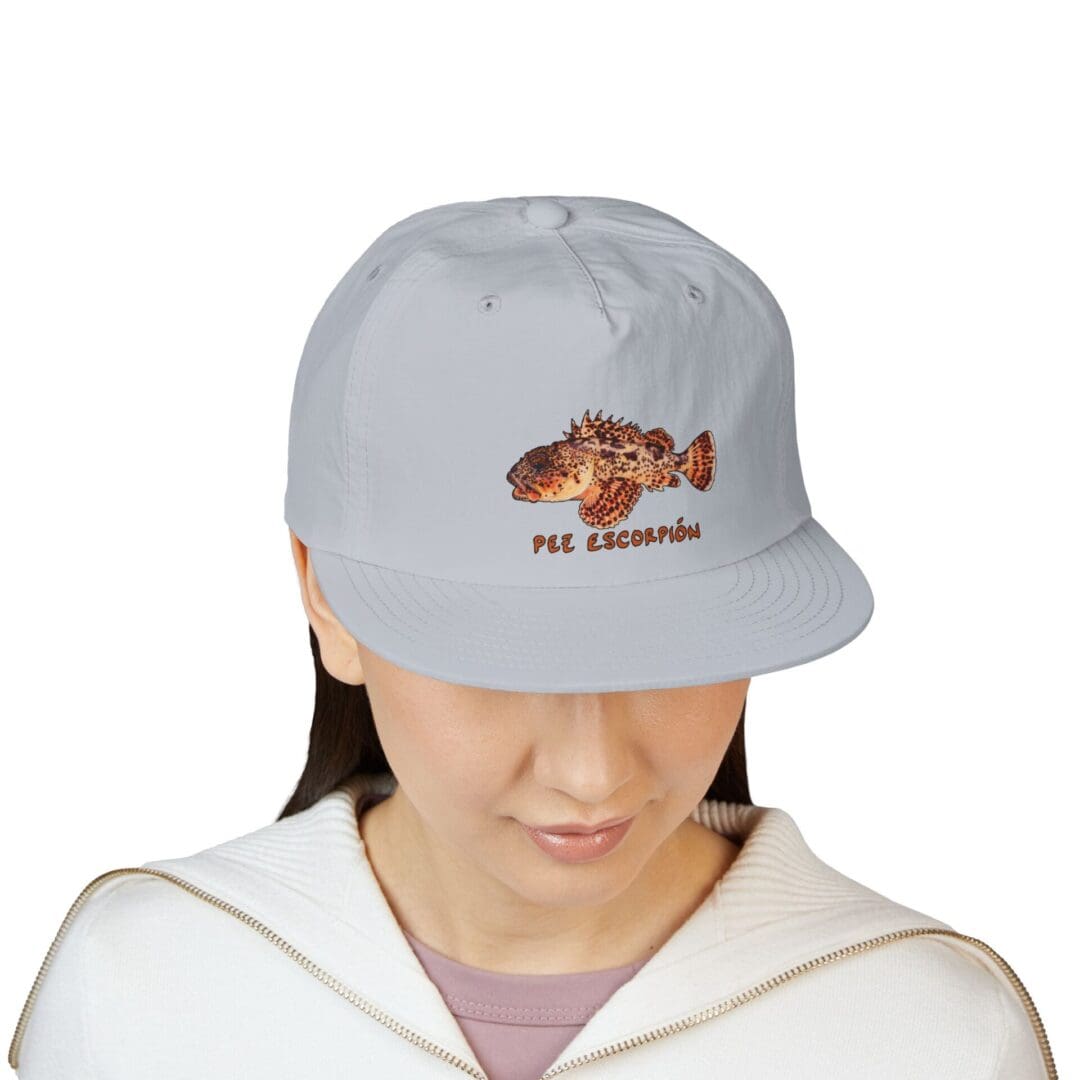 Person wearing a light gray cap with a fish design and text.