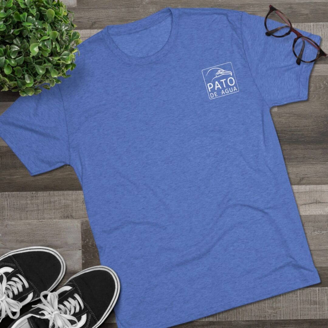 Blue Vato T-shirt laid flat with sneakers and glasses nearby.
