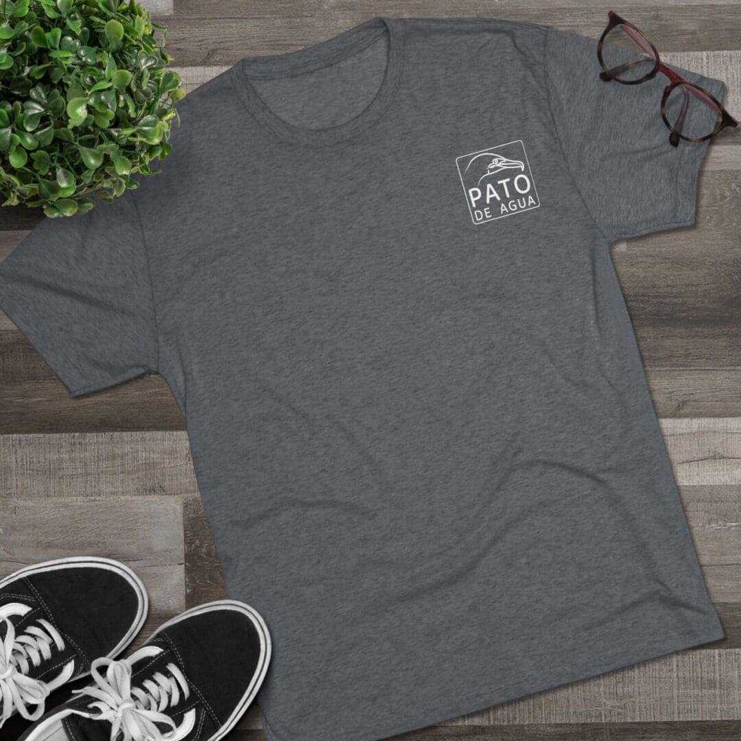 Gray T-shirt with a small white logo on the left chest laid on a wooden surface.